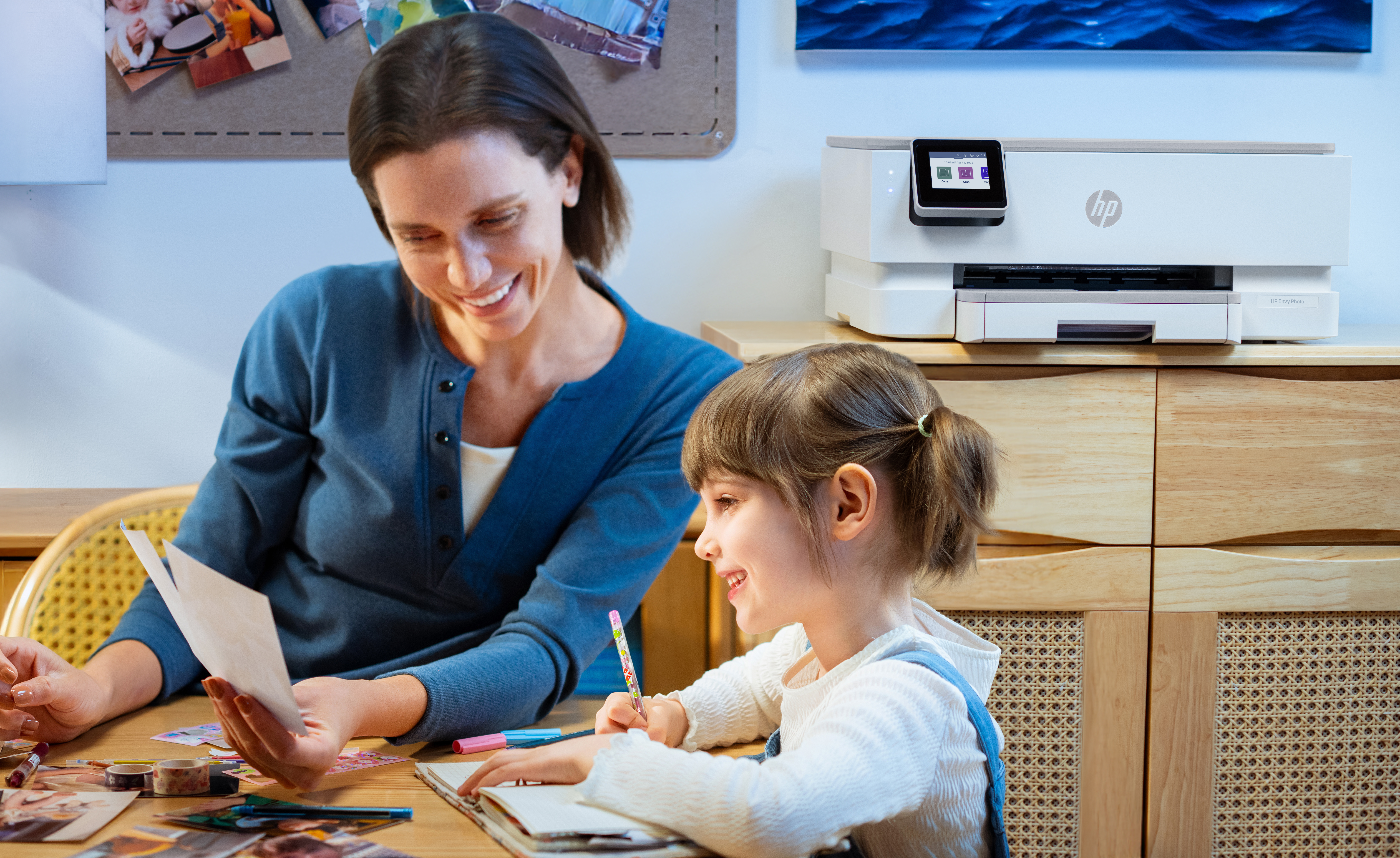 Kobieta i dziewczynka siedzą przy stole, oglądając papiery. Drukarka HP stoi za nimi na drewnianej szafce.