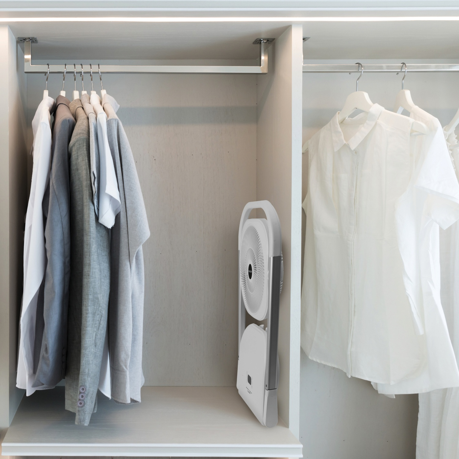All'interno di un armadio bianco, i vestiti sono appesi alle aste. Un ventilatore bianco è piegato e riposto. Sono visibili camicie bianche e grigie e una giacca.