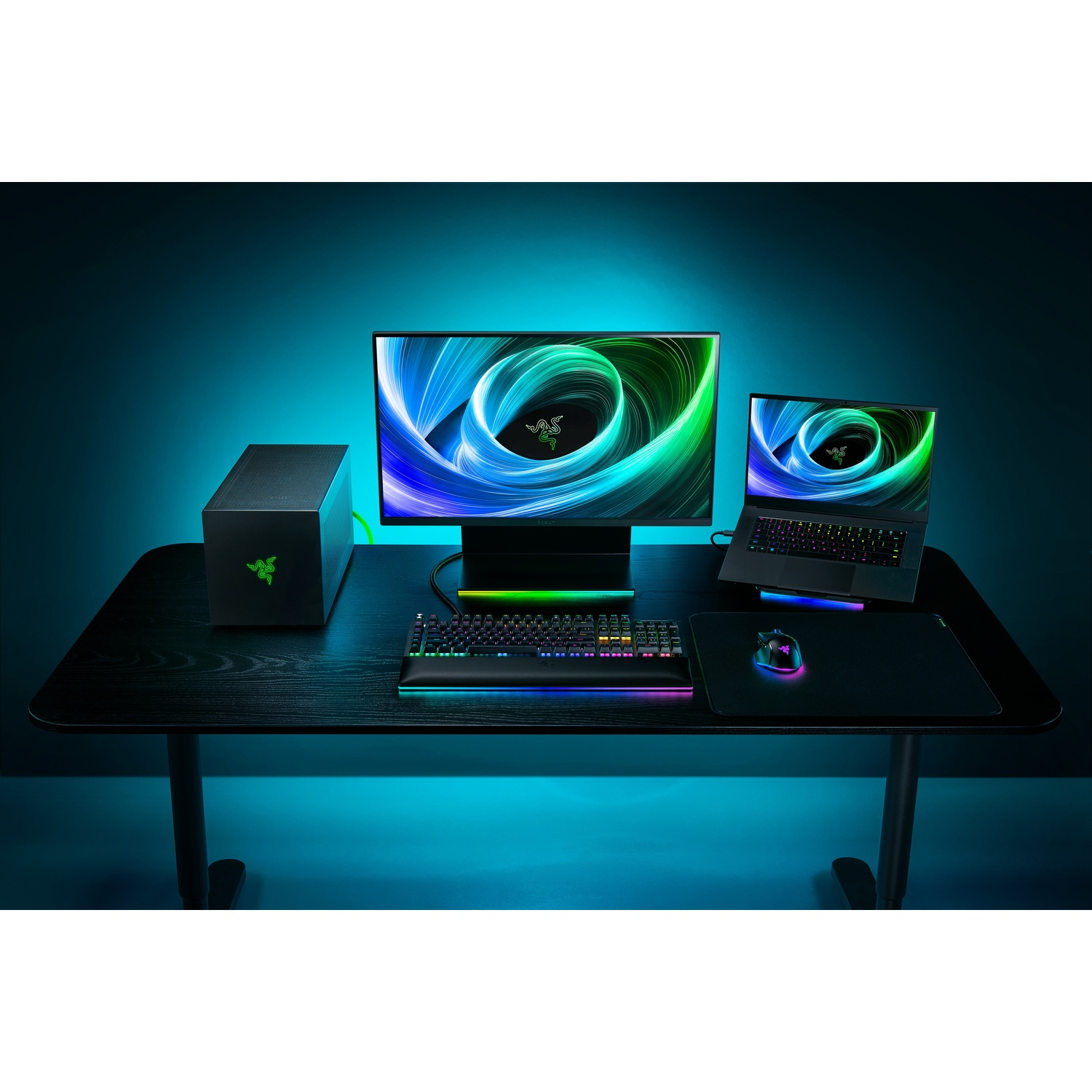 Une configuration de jeu avec un moniteur, un ordinateur portable, un clavier, une souris et un boîtier PC sur un bureau noir, avec le logo Razer.
