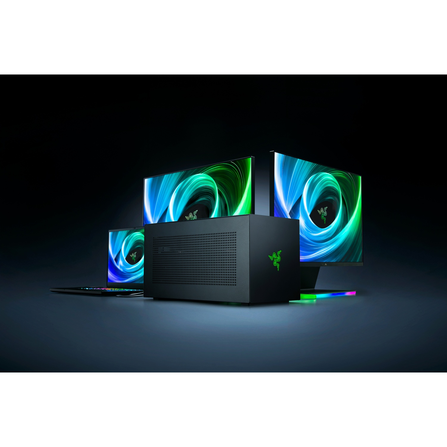 Une configuration informatique noire avec un ordinateur de bureau, des moniteurs et un ordinateur portable avec logos Razer et détails verts.
