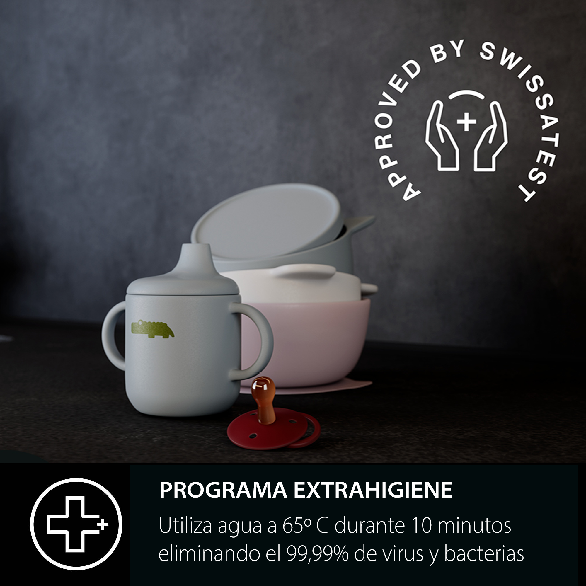 Un vaso gris para bebé con un cocodrilo verde, un chupete y cuencos sobre una superficie negra. Un logo blanco en la parte superior.