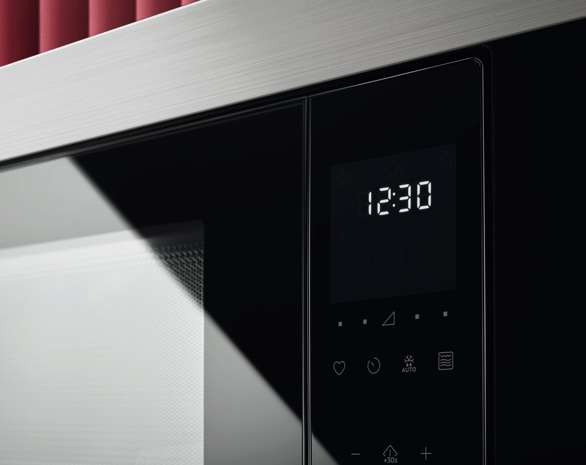 Primer plano de un horno microondas. La pantalla muestra 12:30. Hay botones e iconos debajo de la pantalla en un panel negro.