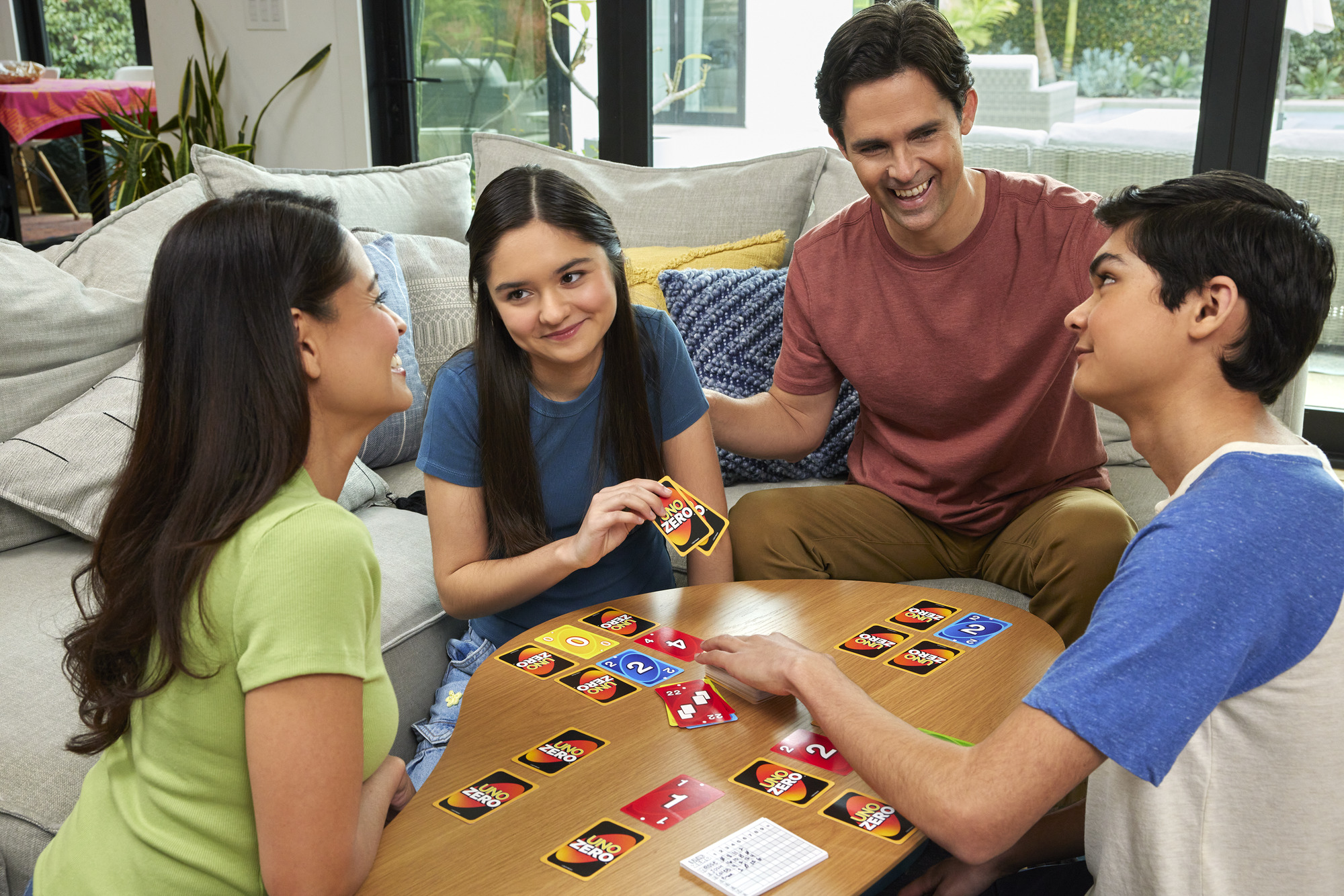 Familie spielt ein Kartenspiel, Uno Zero, an einem Tisch. Menschen lächeln. Karten sind auf dem Tisch und in den Händen sichtbar.