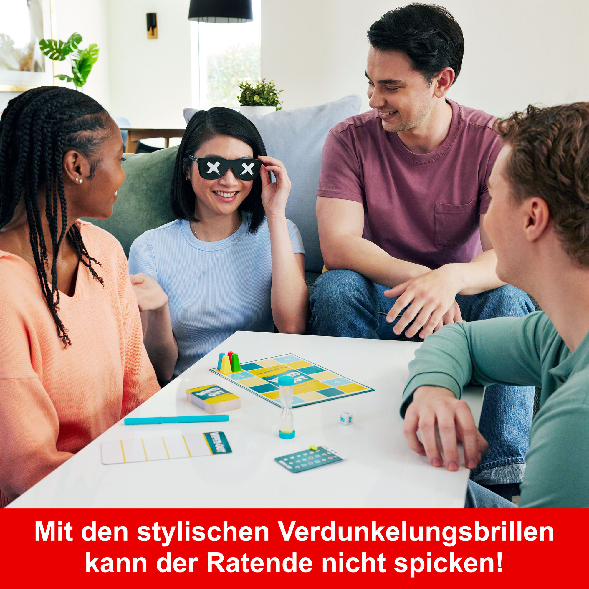Vier Personen spielen ein Brettspiel. Eine Frau trägt eine Sonnenbrille mit X'en auf den Gläsern. Ein Spielbrett, Karten und Würfel liegen auf dem Tisch.