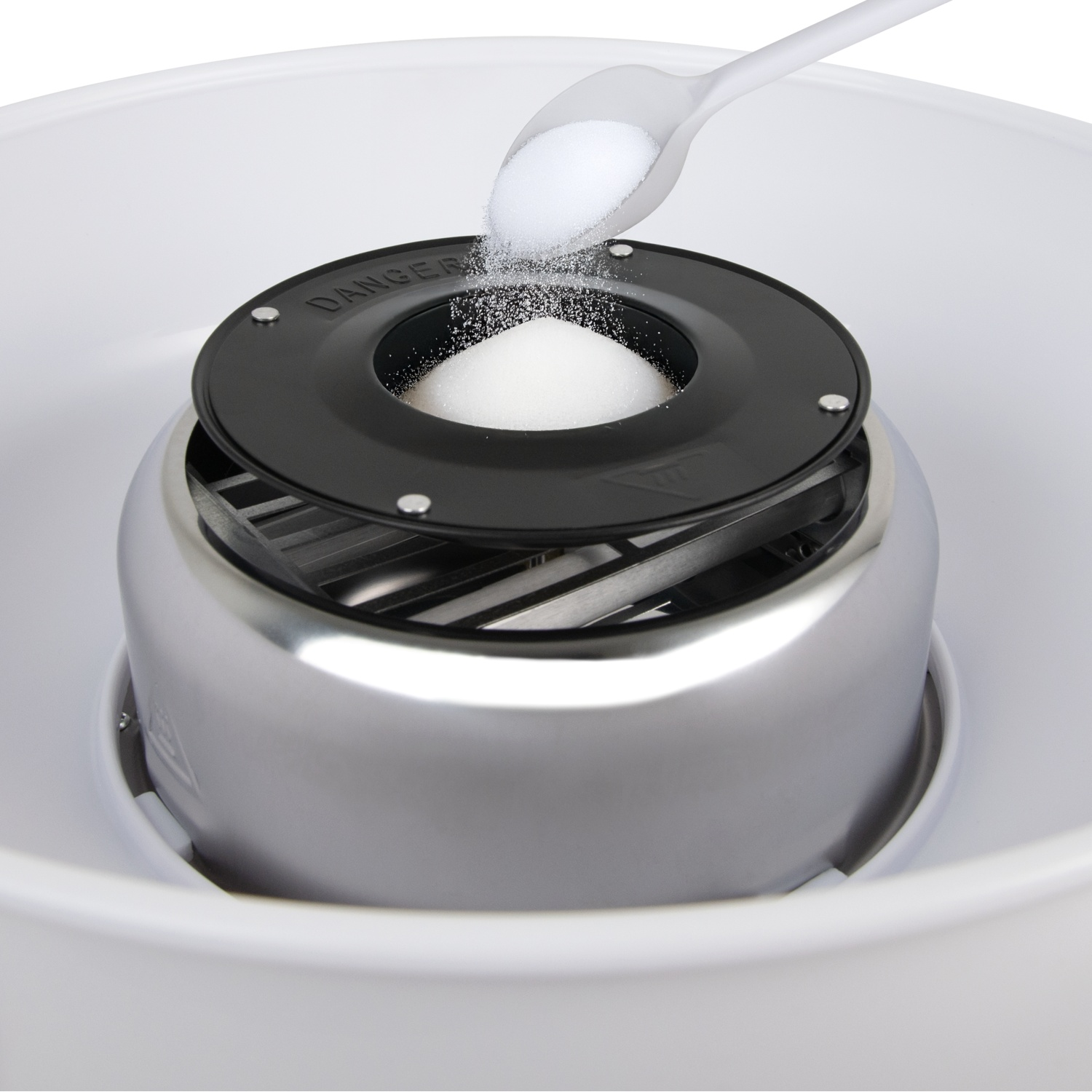 A cotton candy machine with sugar being poured in. Machine is silver and black, with a white bowl around it.