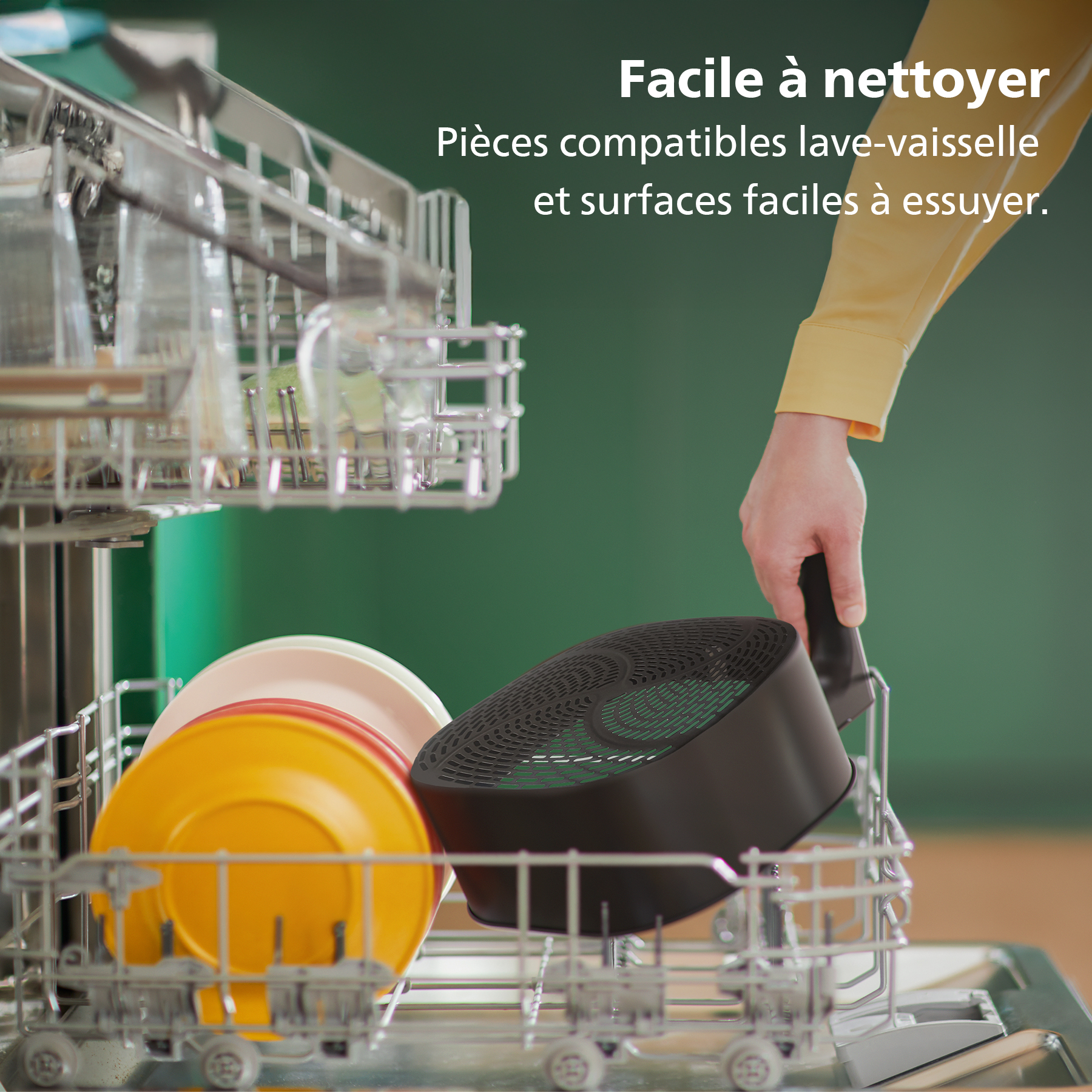 Lave-vaisselle avec de la vaisselle, une personne tenant une pièce noire de l'appareil. Assiettes jaunes, rouges et blanches dans le support.