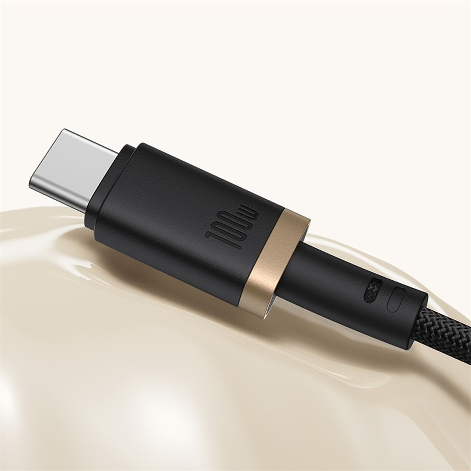 Primer plano de un cable USB-C negro con un conector plateado. El cable tiene un anillo dorado y una sección trenzada. El fondo está borroso.