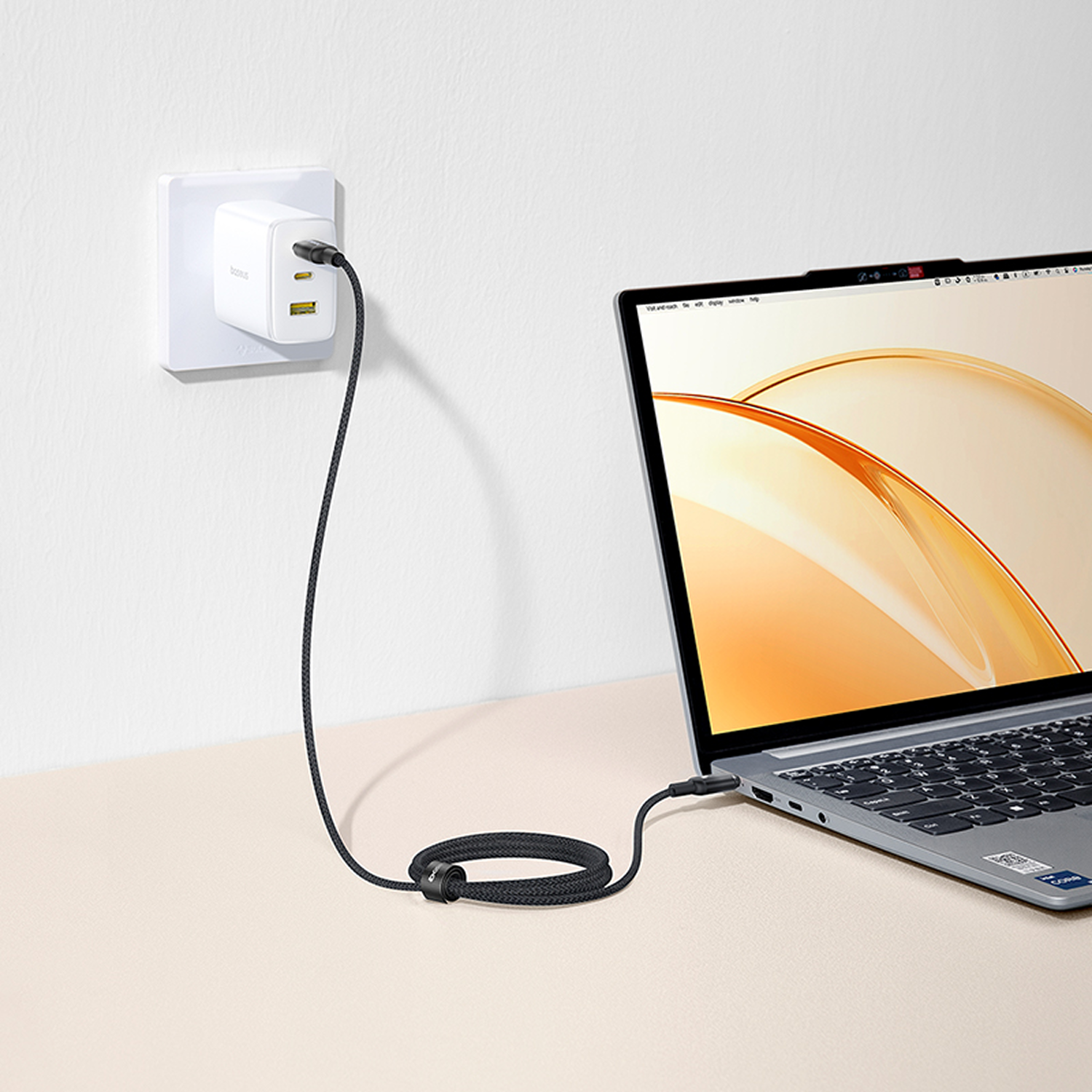 Carga de portátil con un cable negro conectado a un adaptador de corriente blanco enchufado a una toma de corriente. El portátil está abierto.