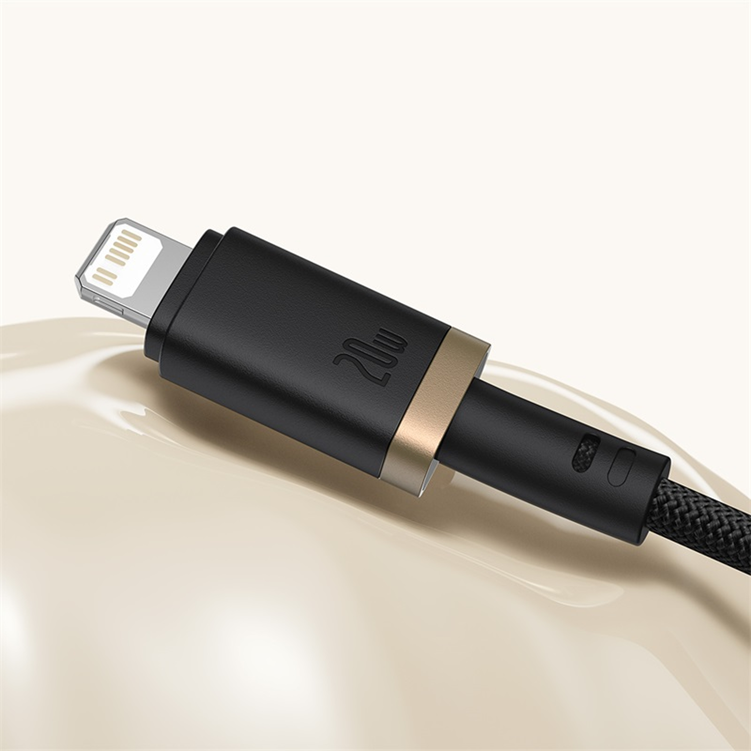 Un cable de carga negro y dorado. El cable tiene un conector Lightning, un cuerpo negro con '20W' y un cable trenzado.