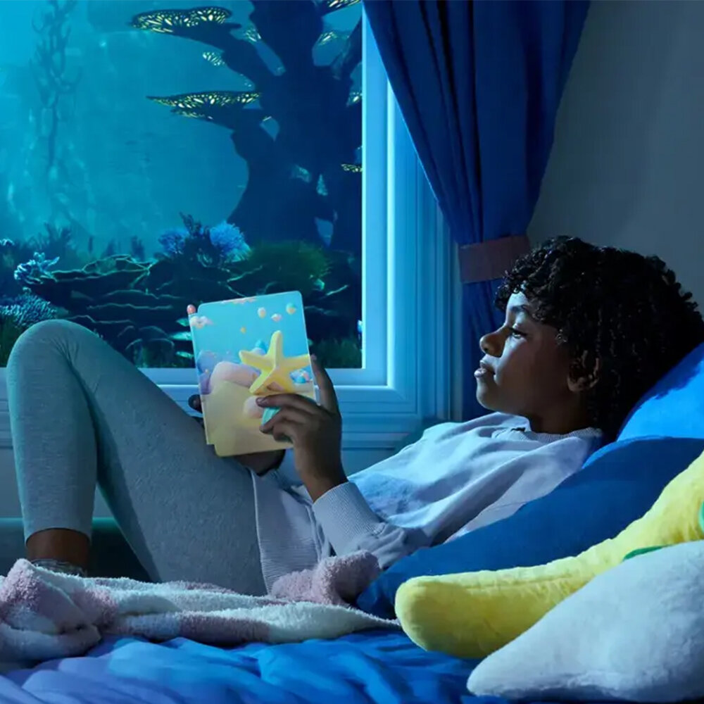 Dziewczyna czyta książkę z rozgwiazdą na okładce, leżąc na łóżku. Za oknem scena podwodna.
