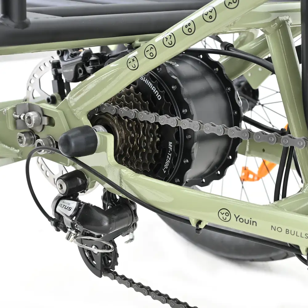 Primer plano de la rueda trasera y la transmisión de una bicicleta. La bicicleta tiene un cuadro verde, cadena, engranajes y componentes Shimano.