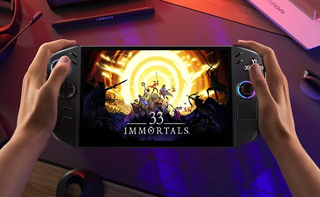 Mains tenant une console de jeu portable affichant le jeu '33 Immortals'. L'appareil est noir, avec un écran et des boutons colorés.
