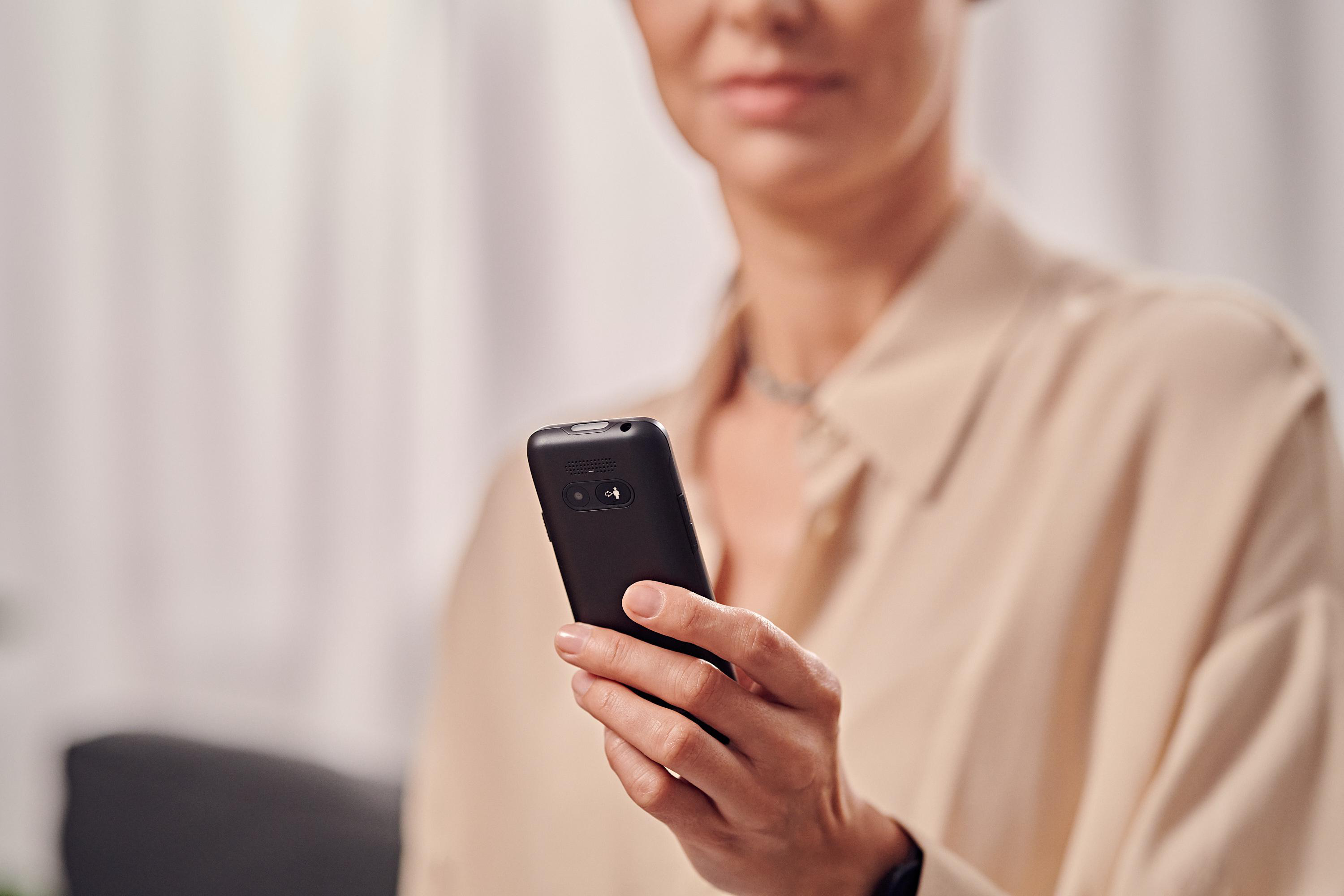Eine Person hält ein schwarzes Smartphone. Die Person trägt ein beiges Hemd.