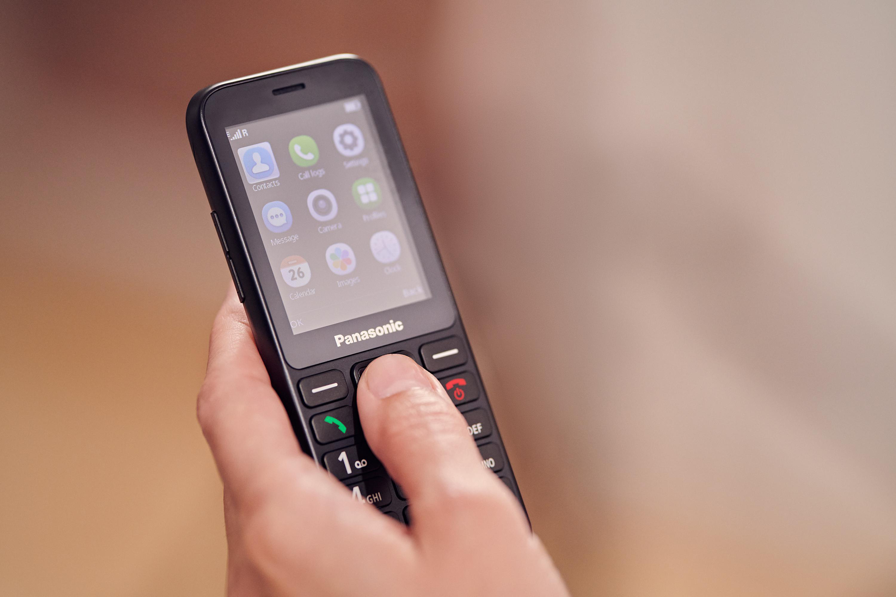 Eine Hand hält ein schwarzes Panasonic-Telefon. Der Bildschirm zeigt Symbole für Kontakte, Nachrichten und Einstellungen.