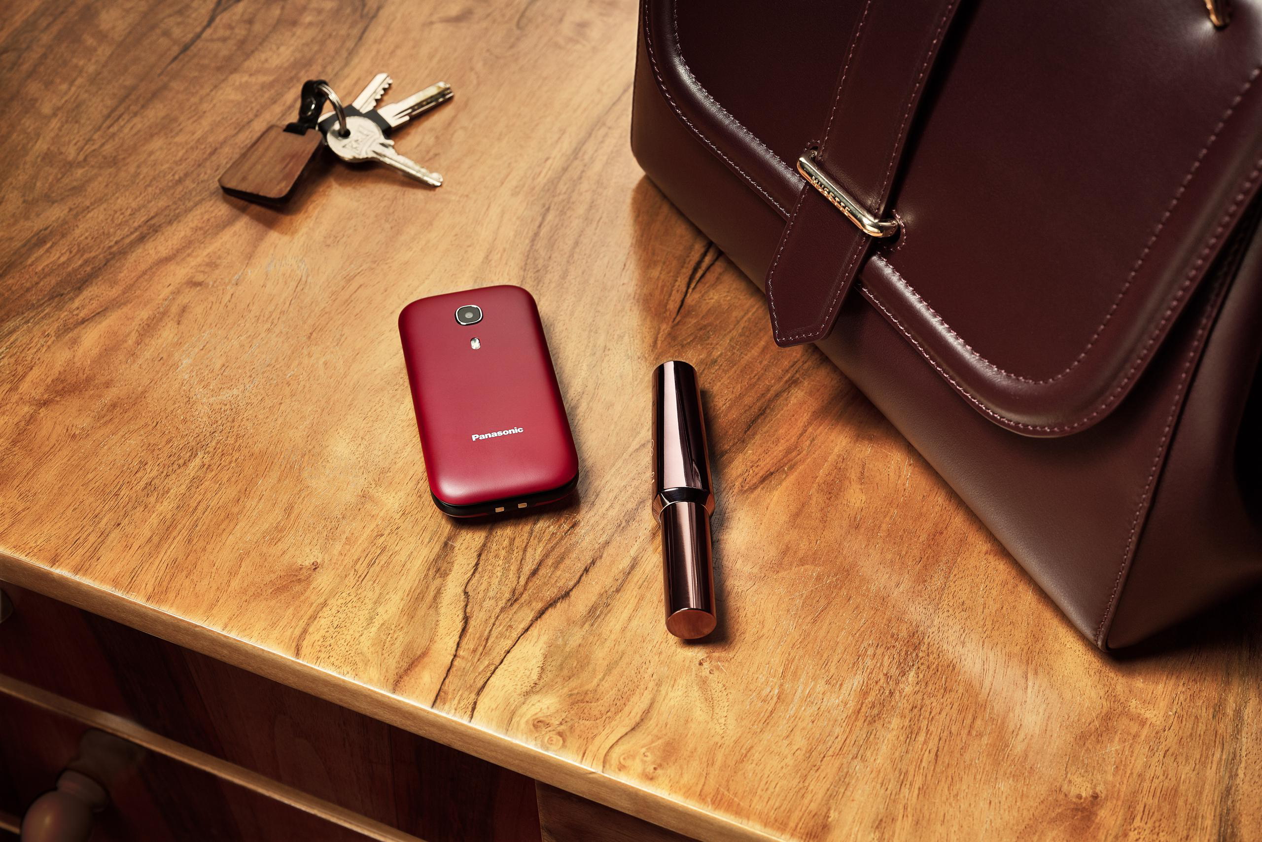 Ein Holztisch mit Schlüsseln, einem roten Telefon, einem Lippenstift und einer braunen Tasche.