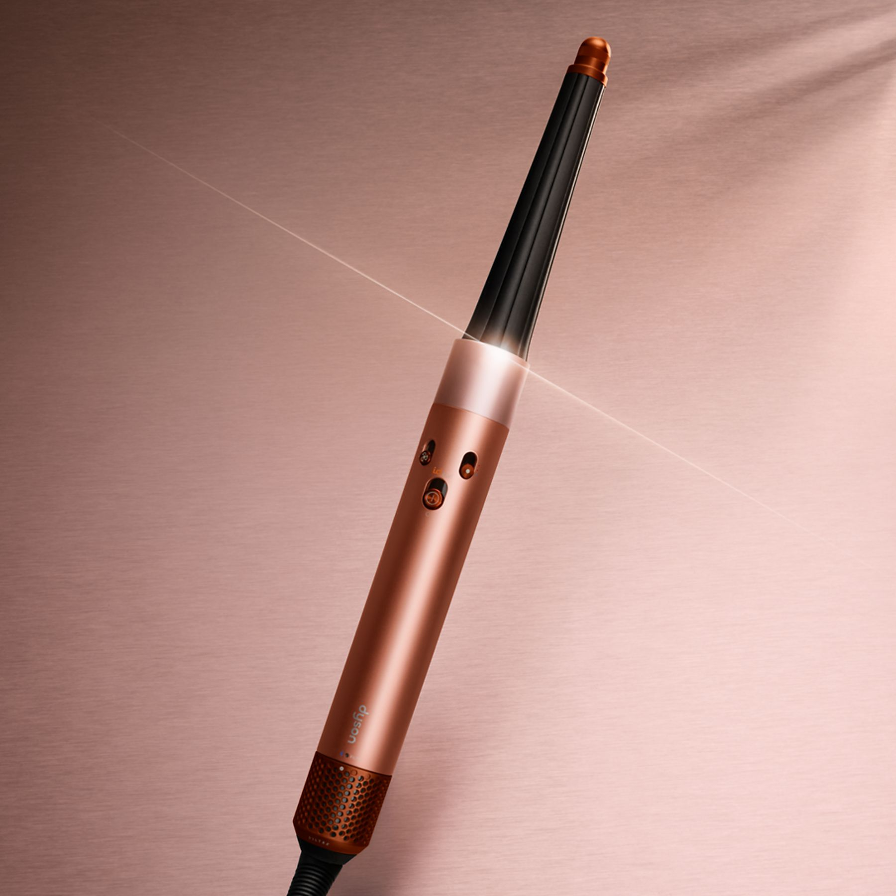 Róża-złota lokówka Dyson na róża-złotej powierzchni, z czarnym uchwytem, nachylona od góry po prawej do dołu po lewej.