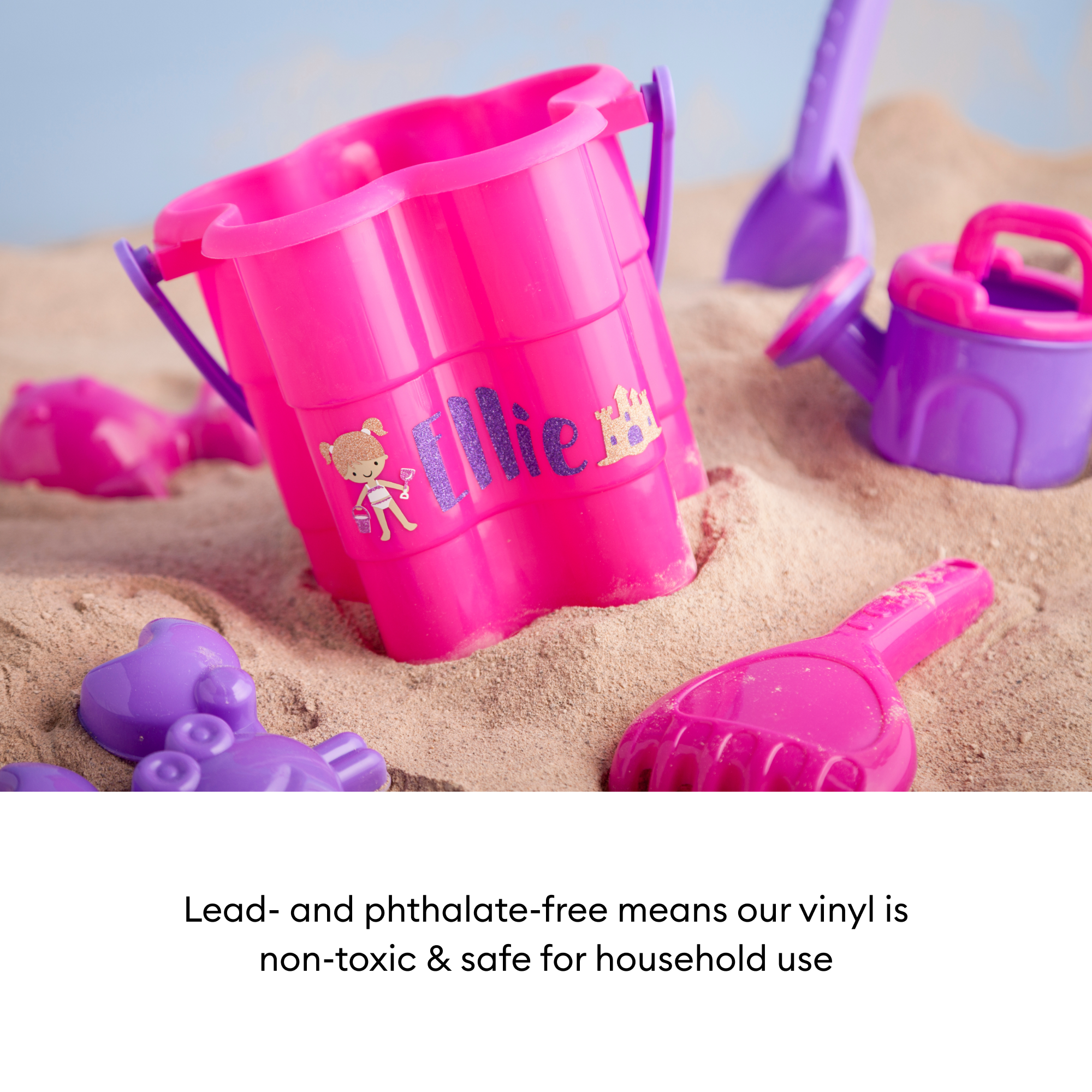 Rosa Sandspielzeug auf Sand. Eimer, Schaufel, Gießkanne und Formen sind sichtbar. Hintergrund ist ein blauer Himmel.