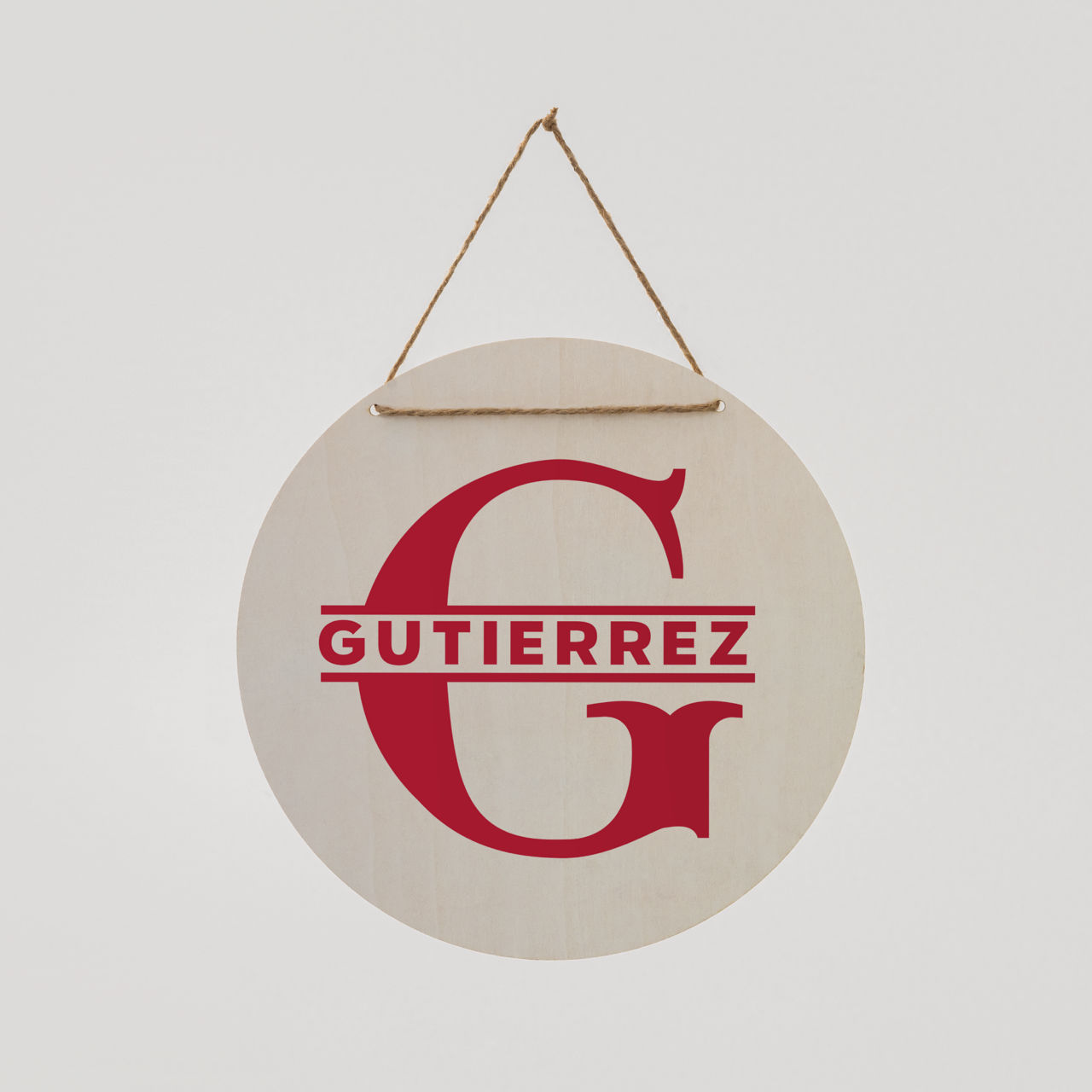 Ein rundes Holzschild mit einem roten 'G' und 'GUTIERREZ' darunter. Es hängt an einem Seil vor weißem Hintergrund.