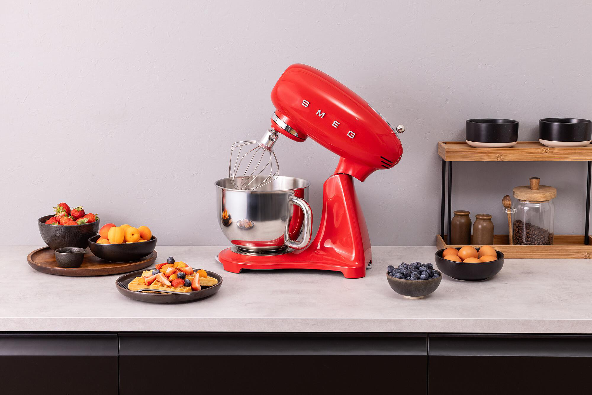 Roter Küchenmixer, Obstschalen, Waffeln und Eier auf einer Arbeitsplatte. Küchenszene.