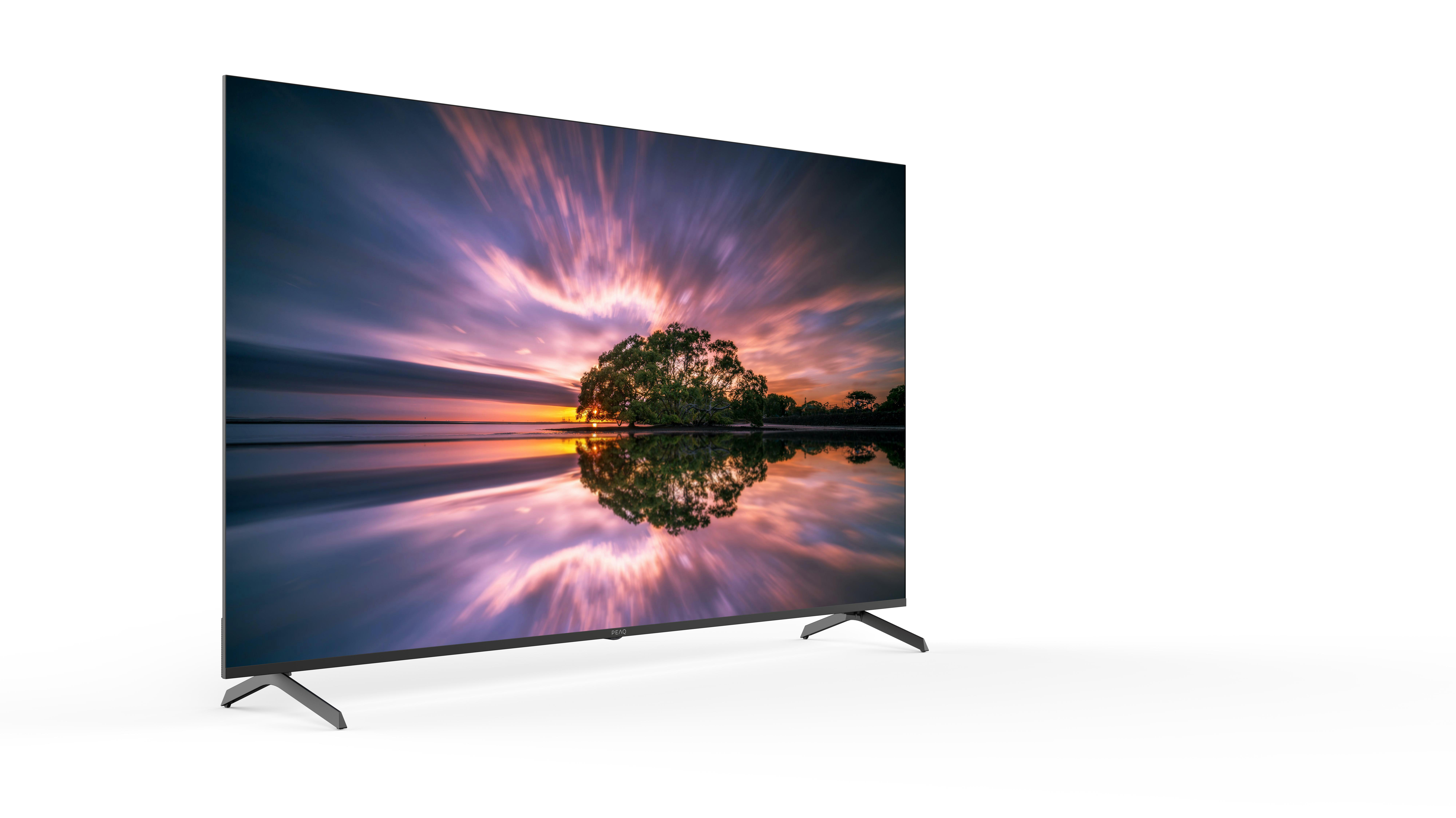 Der Fernseher zeigt eine Sonnenuntergangsszene mit einem Baum im Wasser, der den Himmel widerspiegelt. Der Fernseher steht auf weißem Grund mit schwarzen Beinen.