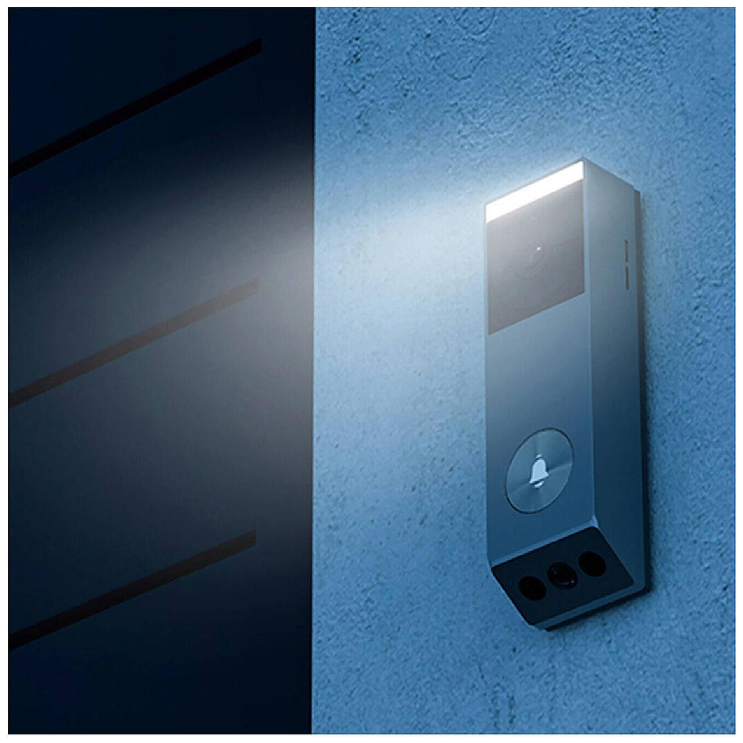 A modern doorbell on a blue wall. It has a light, a bell button, and three small holes. Left: a dark blue wall.