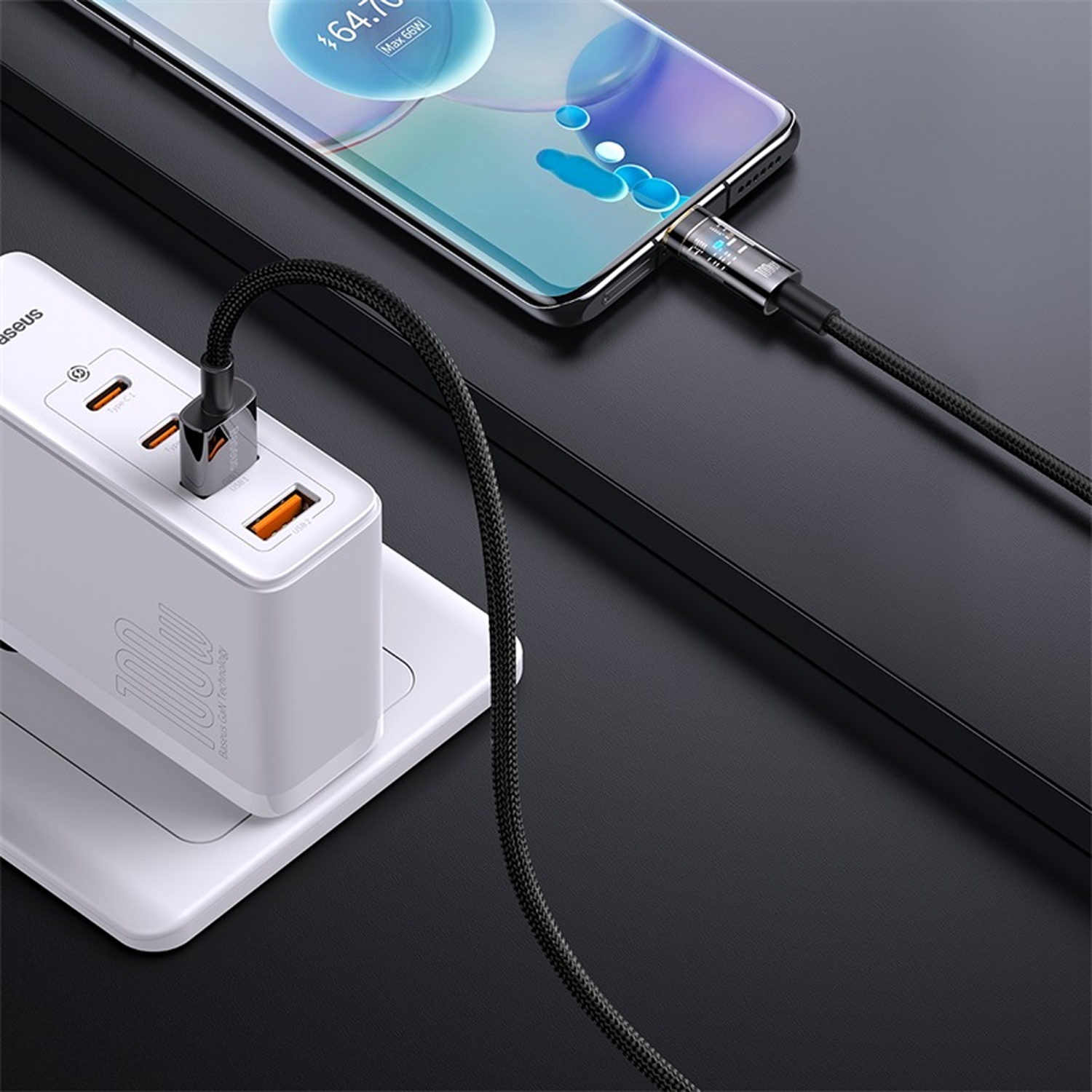 Teléfono cargando. Cable negro conecta el teléfono a un cargador blanco con puertos naranjas. La pantalla muestra el estado.