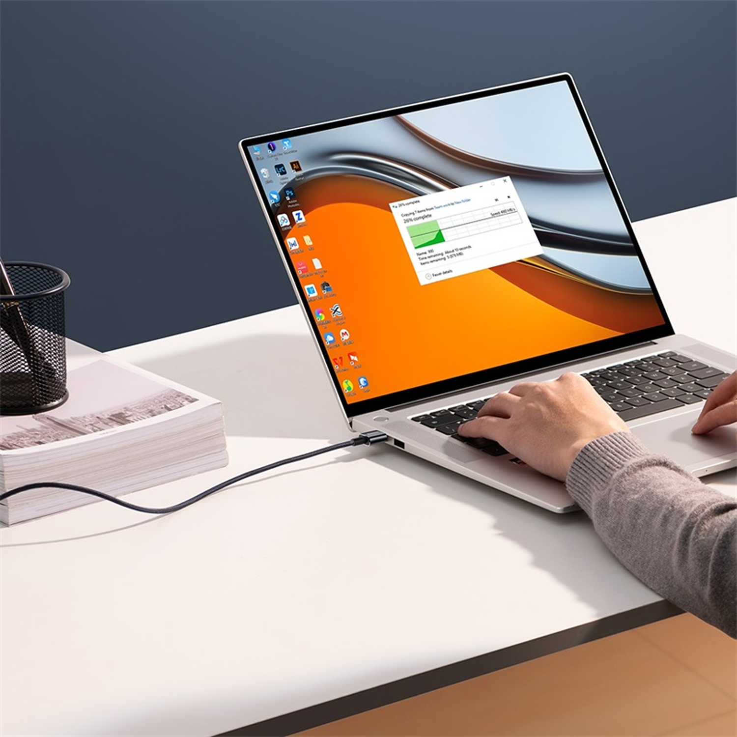 Un portátil sobre un escritorio blanco. Una mano teclea en el teclado. Una ventana muestra una transferencia de archivos en curso.
