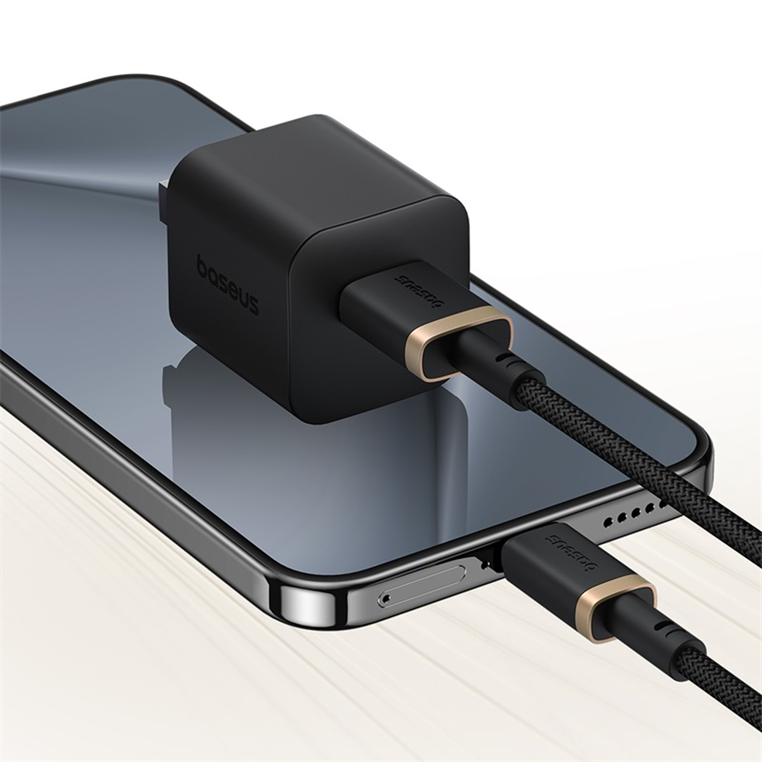 Un cargador Baseus negro conectado a un teléfono. El cargador está enchufado al teléfono, con un cable negro y dorado.