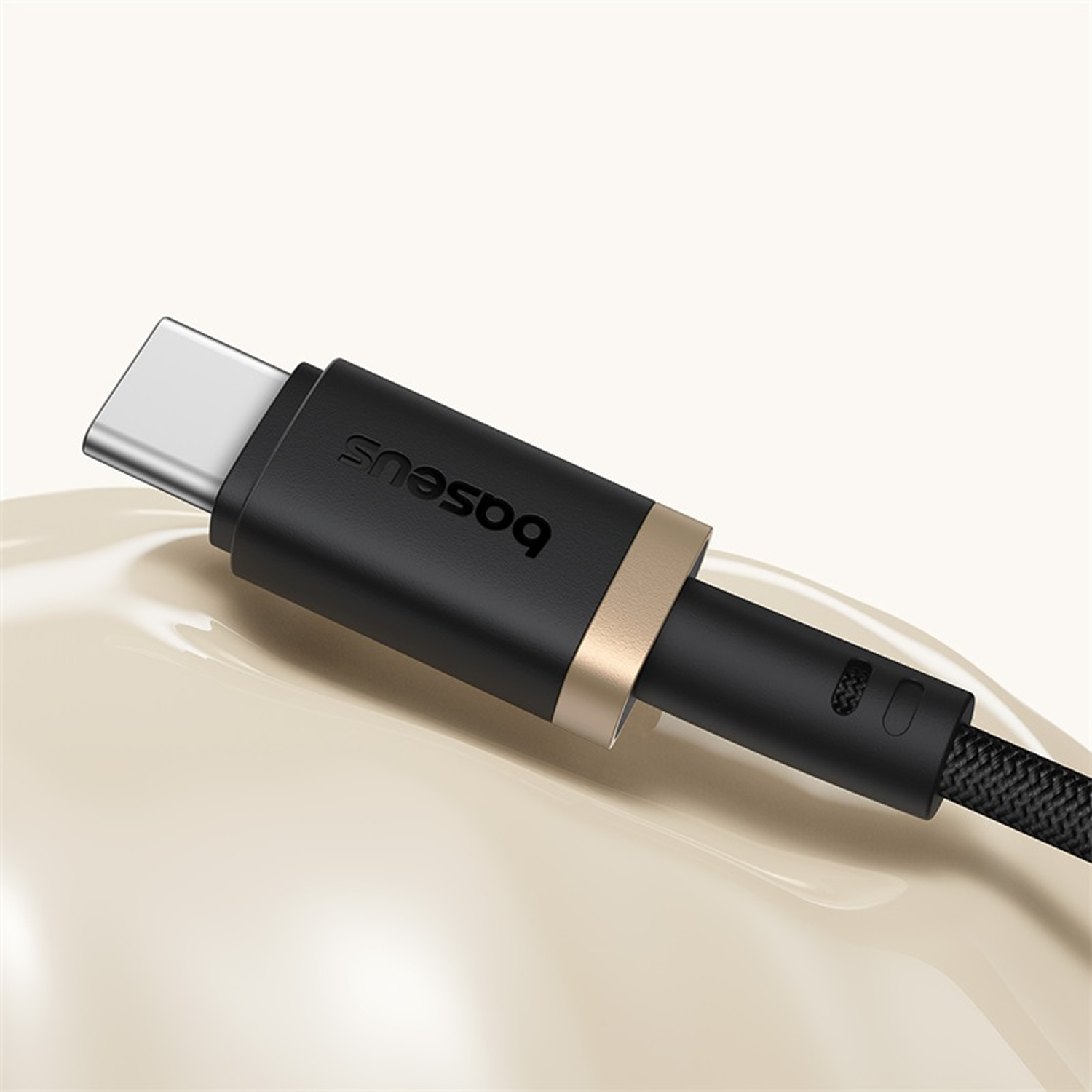 Primer plano de un cable USB-C Baseus negro con un anillo dorado. El fondo es de un color crema suave.