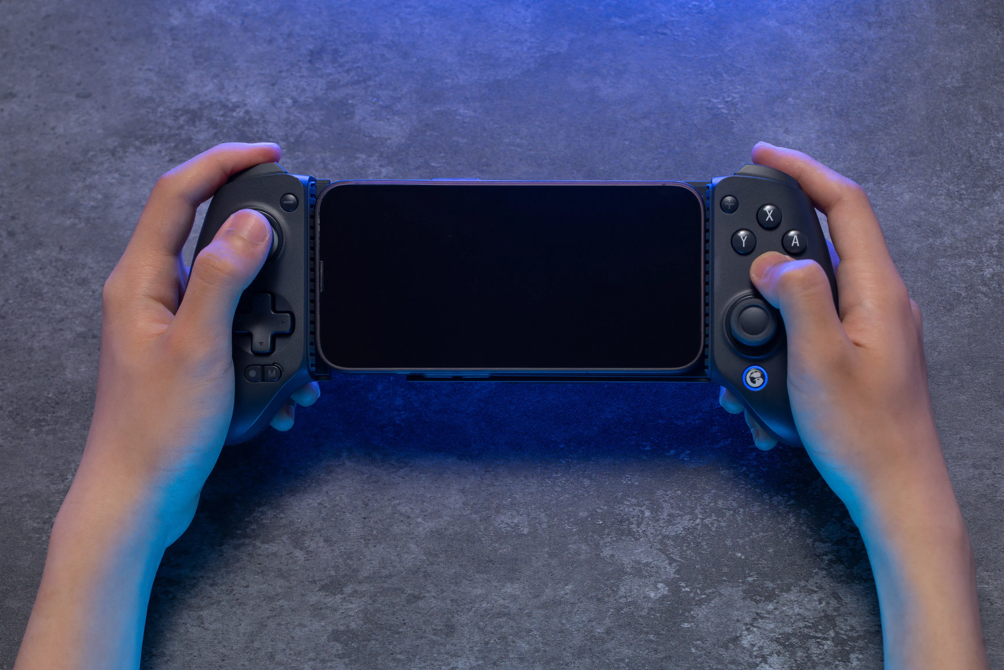 Hände, die ein Smartphone in einem schwarzen Gamecontroller halten. Der Hintergrund ist eine strukturierte graue Oberfläche mit blauem Licht.