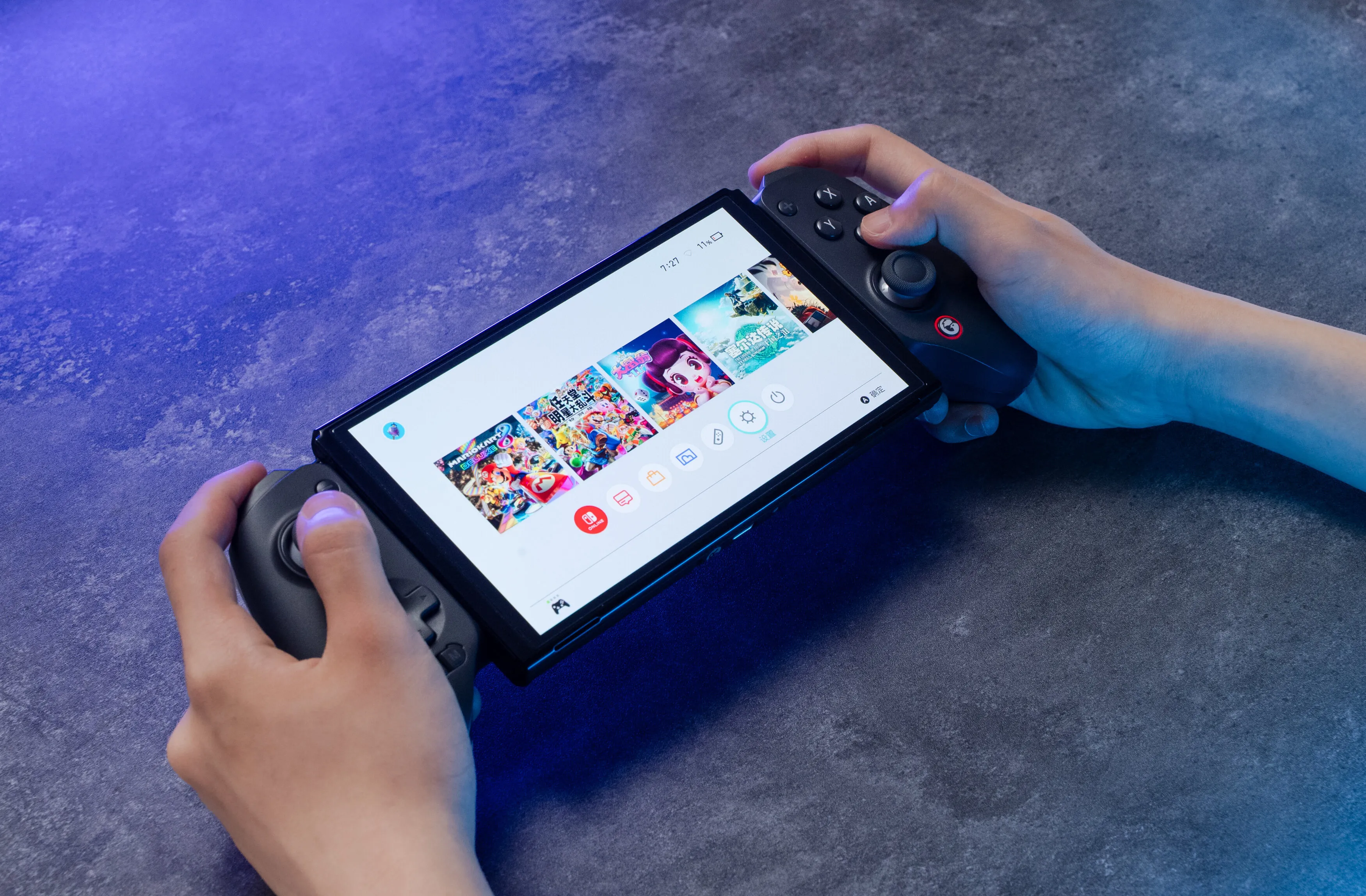 Hände halten eine Handheld-Konsole mit Bildschirm, der Spielauswahlen anzeigt. Graue Controller sind angebracht.