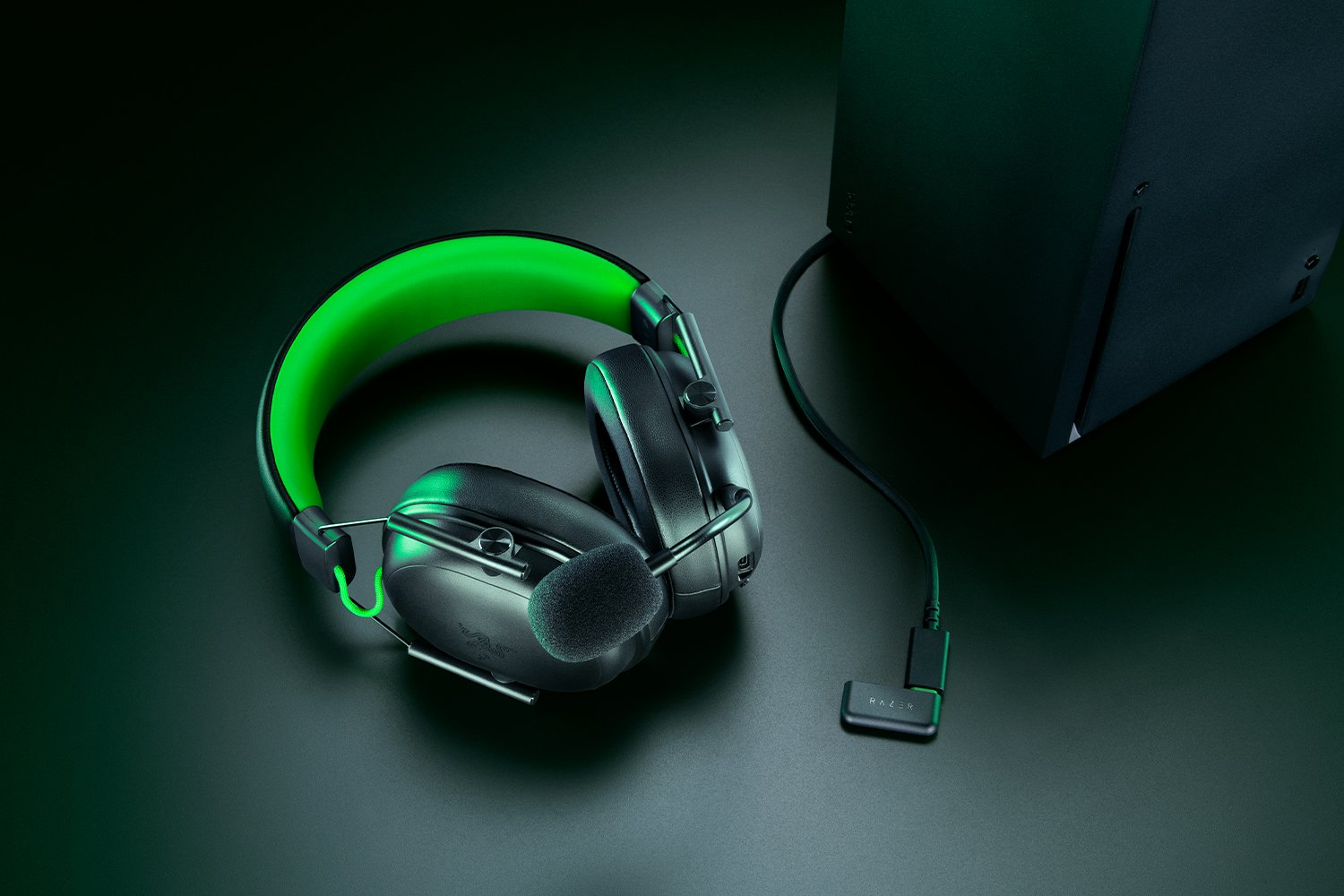 Gaming-Headset mit grünen Akzenten, verbunden mit einer schwarzen Konsole. Razer-Logo sichtbar. Dunkle, elegante Produktaufnahme.