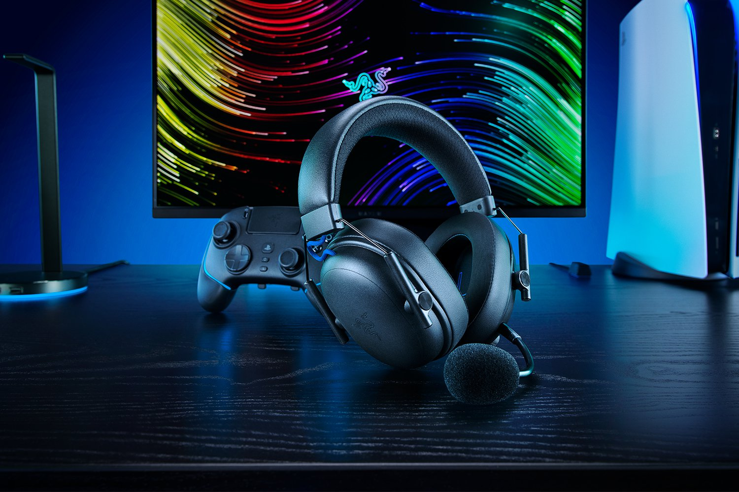 Gaming-Setup mit Headset, Controller und Monitor. Schwarzes Headset vorne. PS5 und Ständer im Hintergrund. Bunter, abstrakter Bildschirm.