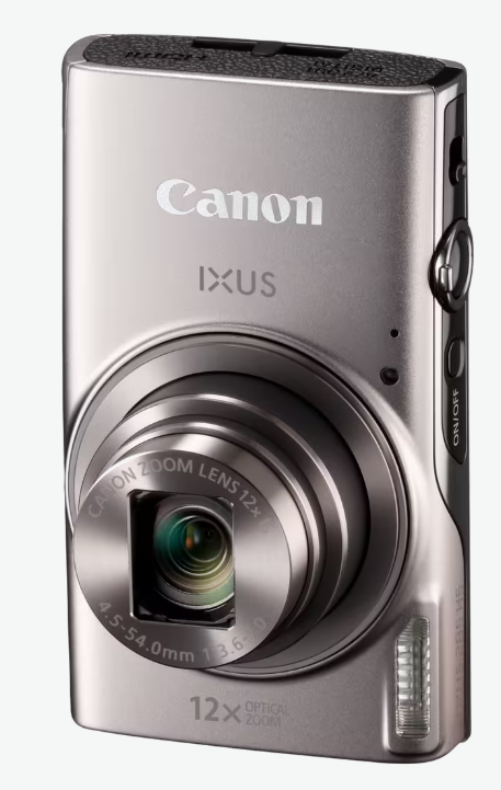 Srebrny aparat cyfrowy Canon IXUS. Posiada obiektyw, przycisk zasilania i 12-krotny zoom optyczny. Tło jest białe.