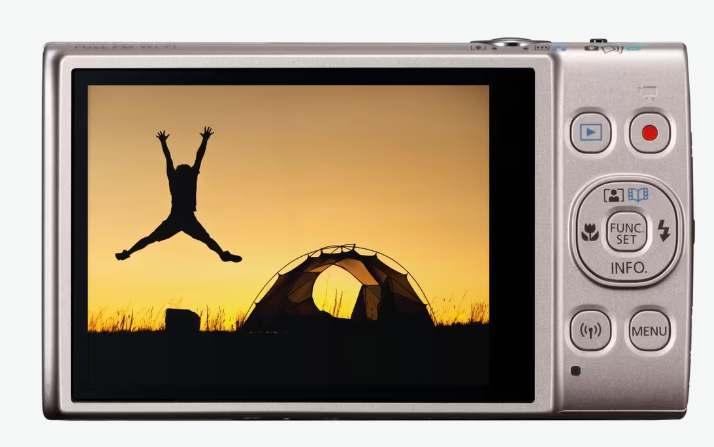 Ekran aparatu pokazuje sylwetkę skaczącej osoby przed namiotem o zachodzie słońca.