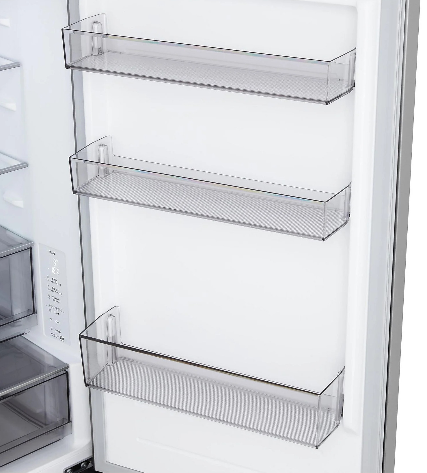 Otwarta komora lodówki z przezroczystymi plastikowymi półkami. Widoczne trzy półki. Białe wnętrze z cyfrowym wyświetlaczem po lewej stronie.
