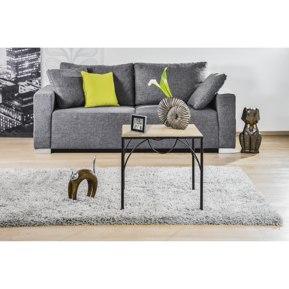 Wohnzimmer mit grauem Sofa, Teppich, Holztisch, Katzen- und Hundestatuen und einer dekorativen Vase. Auf dem Tisch steht eine Uhr.
