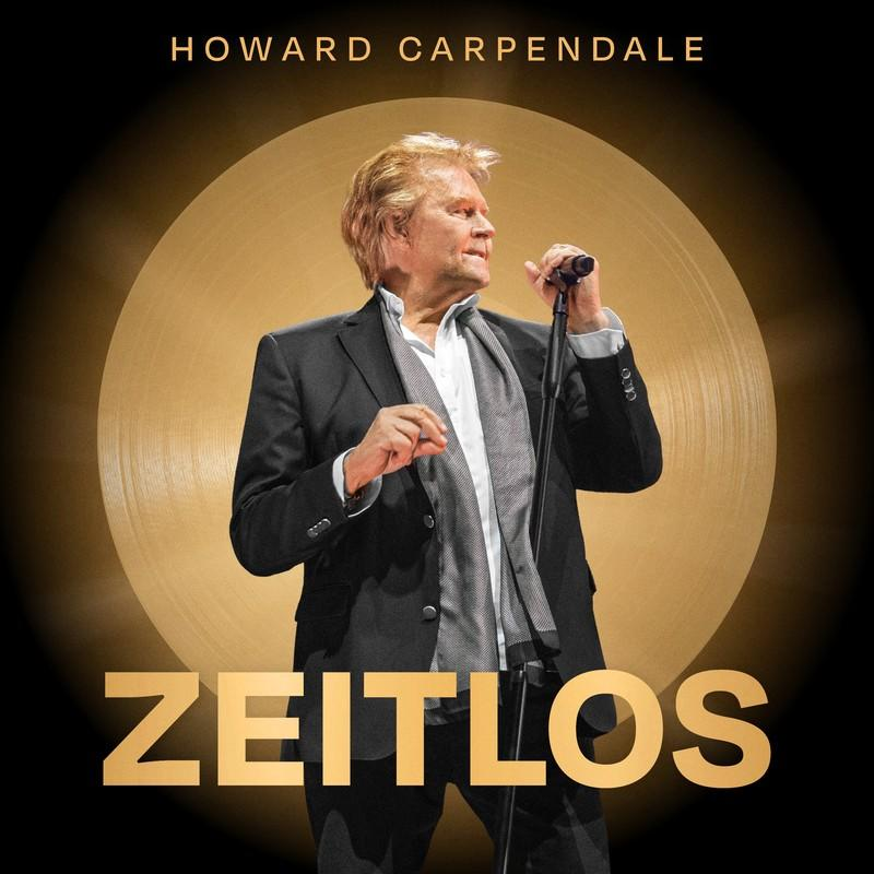 Howard Carpendale steht mit Mikrofon, schwarzem Anzug, goldenem Hintergrund und dem Wort 'ZEITLOS'.