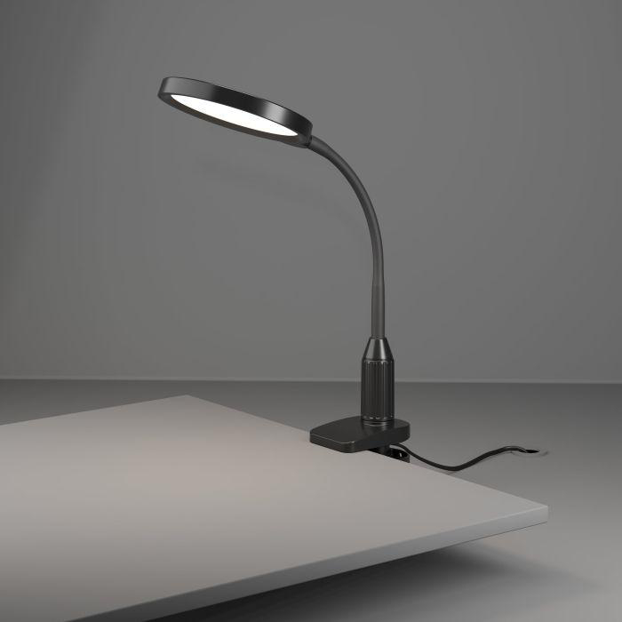 Eine schwarze Schreibtischlampe mit rundem Leuchtkopf ist an einem hellgrauen Schreibtisch befestigt. Der Hintergrund ist grau.