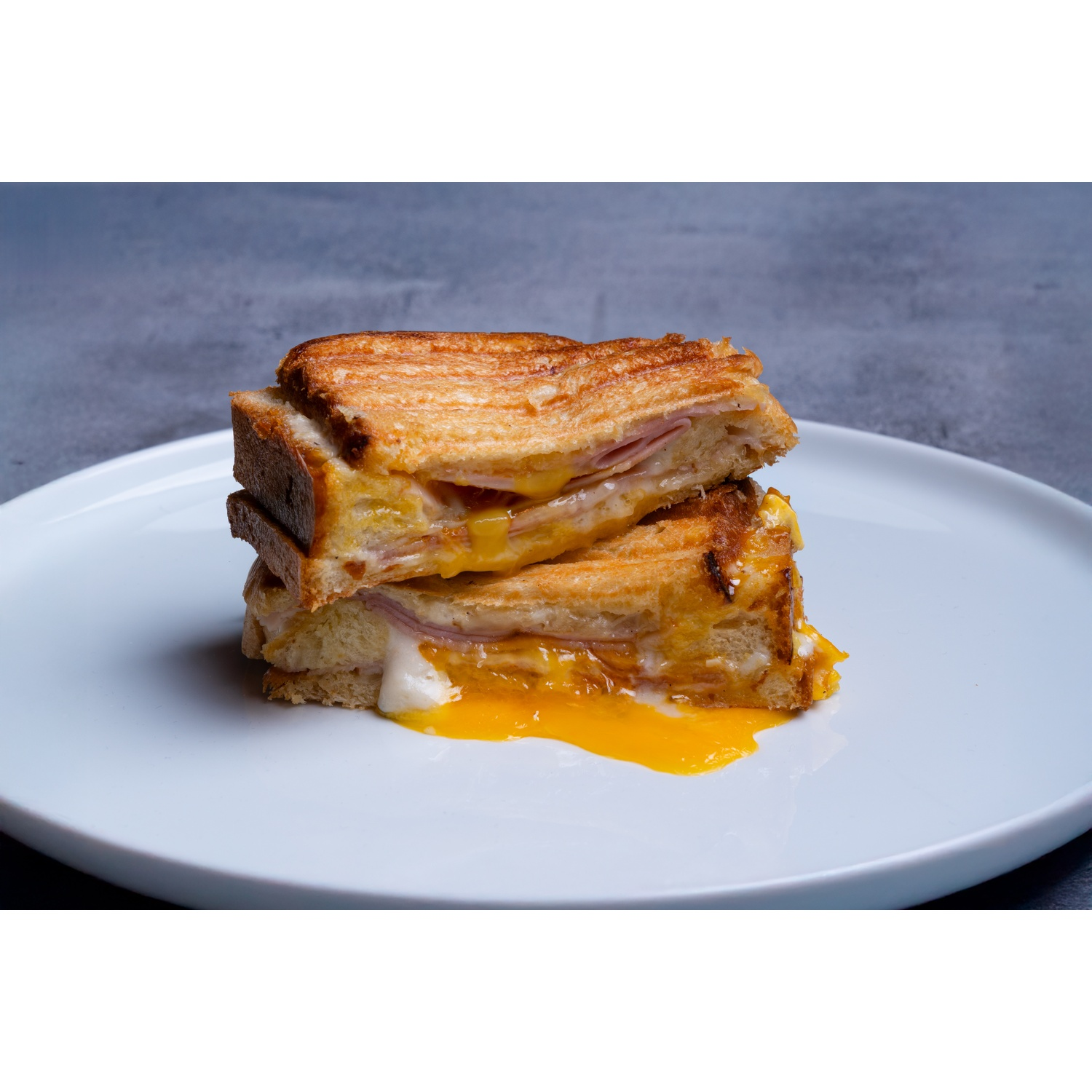 Due metà di un sandwich al formaggio grigliato con prosciutto su un piatto bianco. Tuorlo d'uovo giallo sgocciolante.