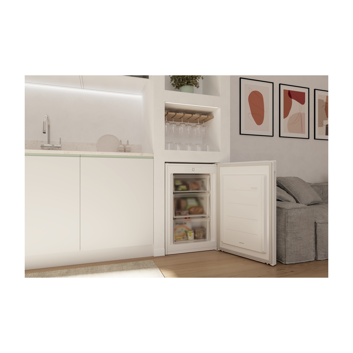 Frigorifero aperto, che mostra cibo all'interno. Ambiente cucina con mobili bianchi e divano grigio sullo sfondo.