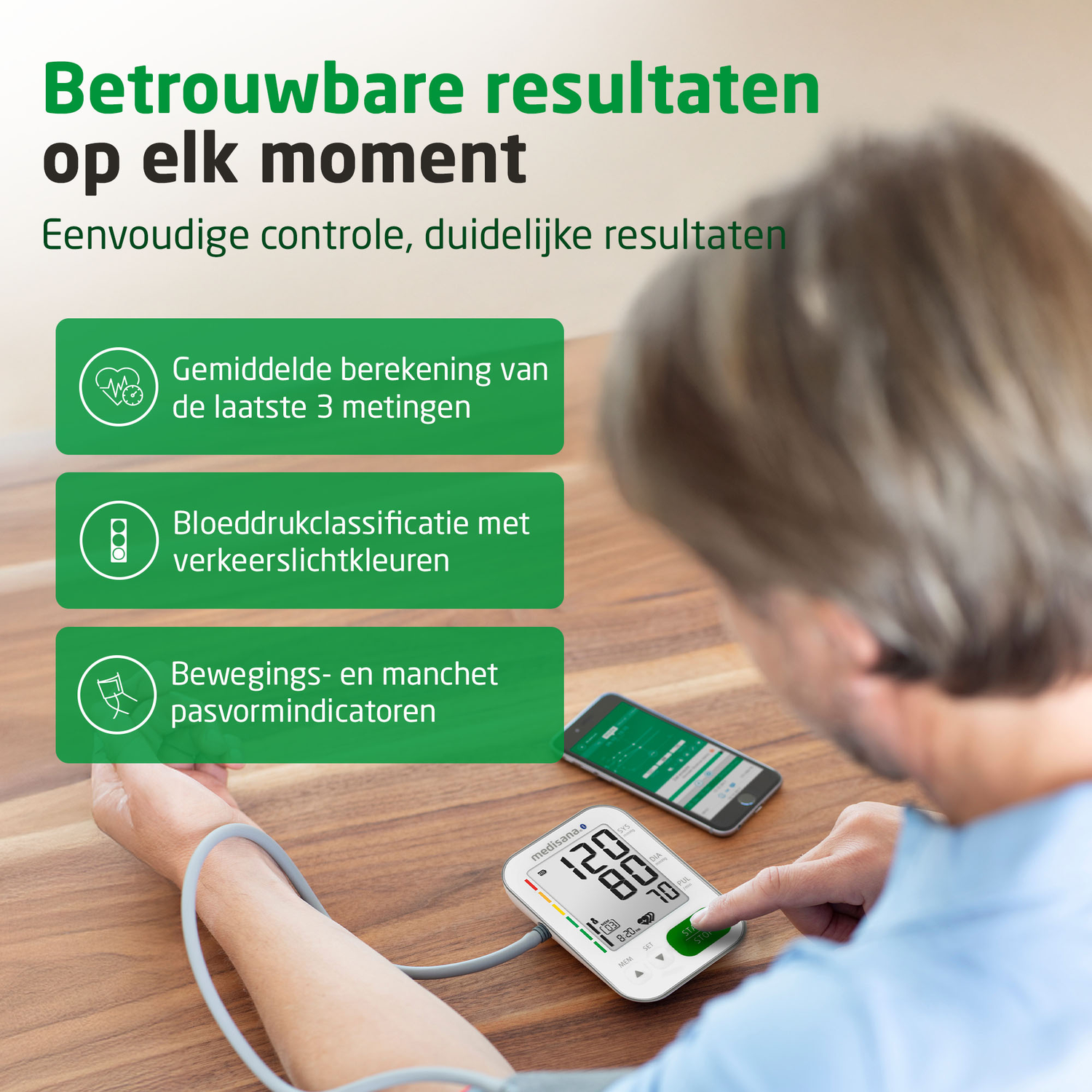 Een persoon gebruikt een bloeddrukmeter. Het scherm toont metingen. Een smartphone en Nederlandse tekst zijn ook zichtbaar.