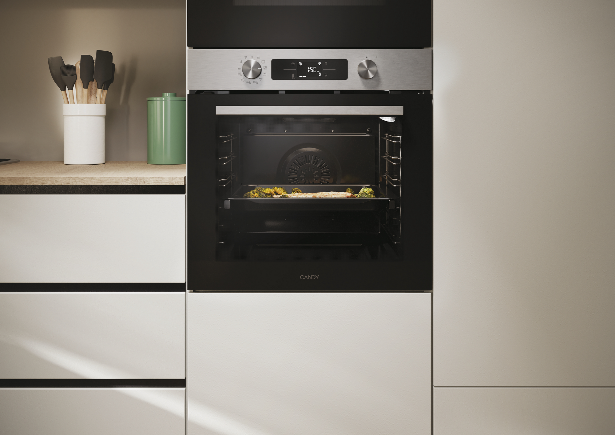 Un horno con comida dentro. El horno está empotrado en un mueble de cocina. Hay utensilios y un recipiente en la encimera.