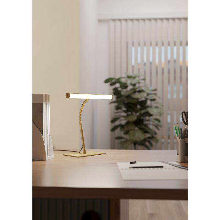 Eine Schreibtischlampe mit goldenem Fuß und Arm steht auf einem Holztisch. Im Hintergrund sind eine Pflanze und Jalousien.