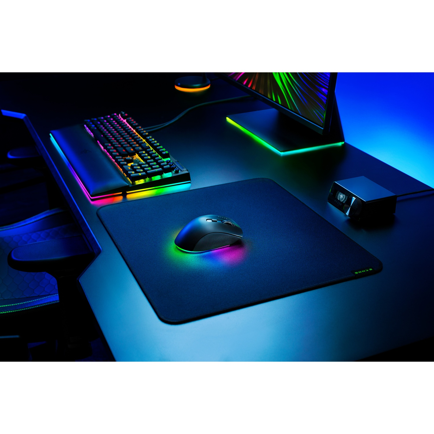 Configuration de jeu avec clavier, souris, tapis de souris et moniteur. Le tout est éclairé par des lumières RVB colorées sur un bureau noir.