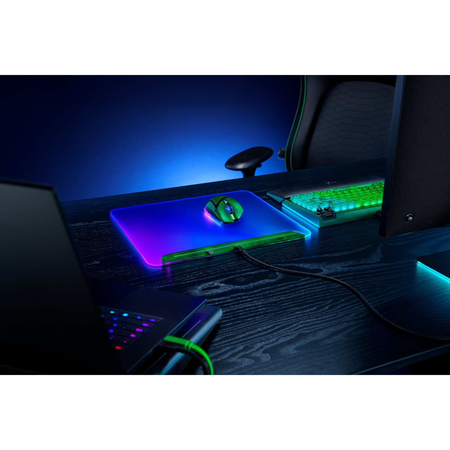 Gaming-opstelling met oplichtende muis, toetsenbord en muismat op een donker bureau. Een laptop is ook zichtbaar.