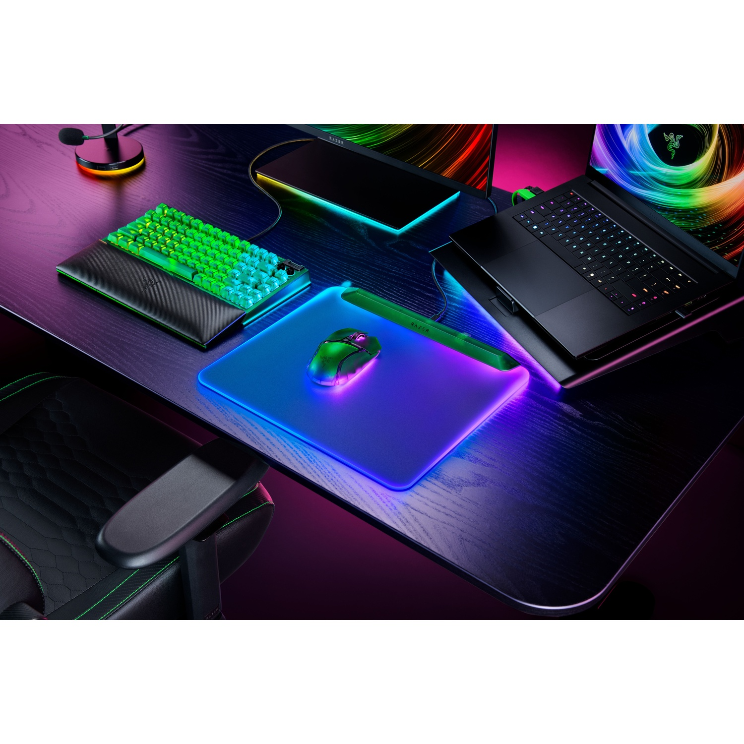 Gaming setup. Inclusief een groen toetsenbord, muis en laptop op een houten bureau. Het bureau heeft ook een gaming muismat en een stoel.