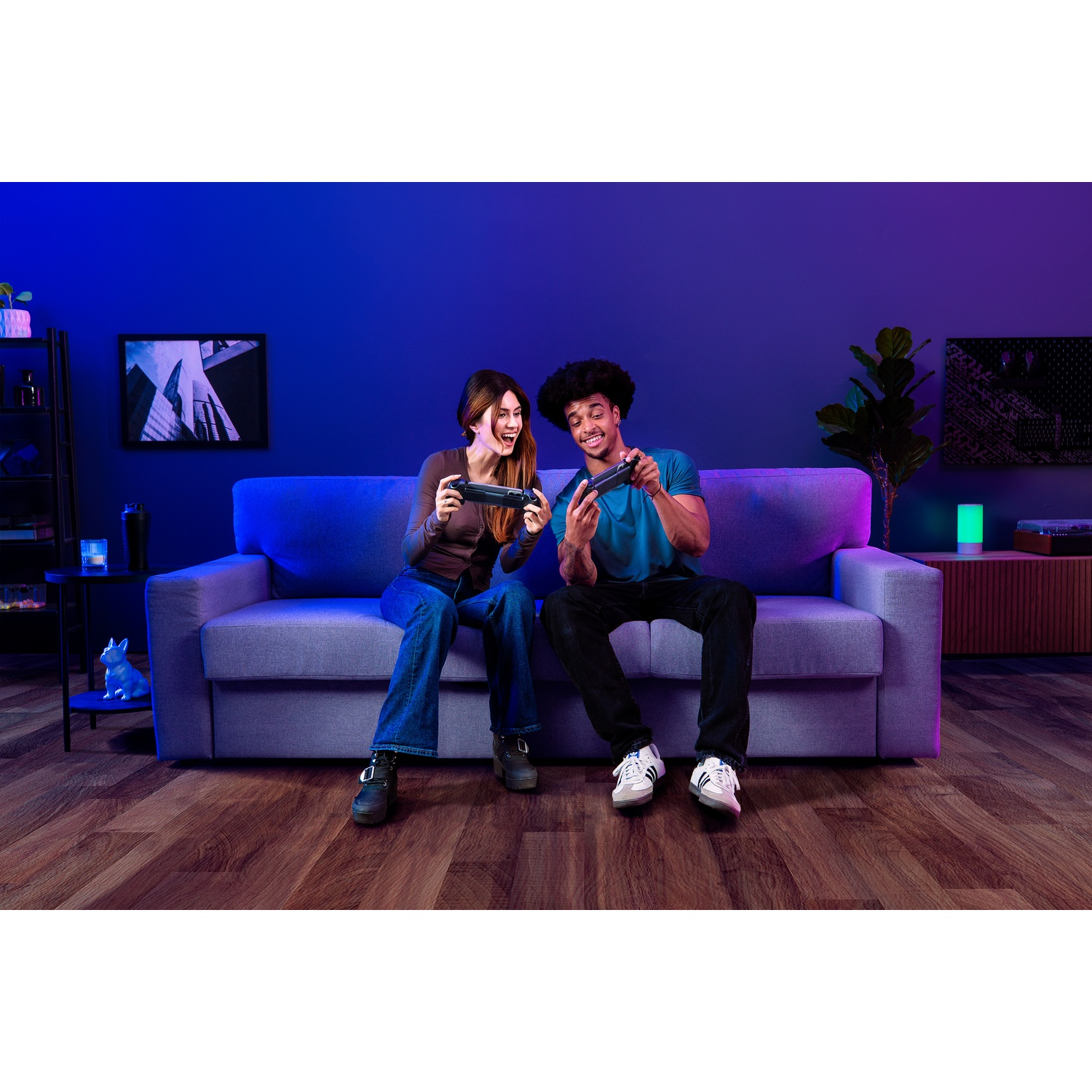 Twee mensen zitten op een bank en spelen videogames met controllers. Ze lachen en kijken naar het scherm.