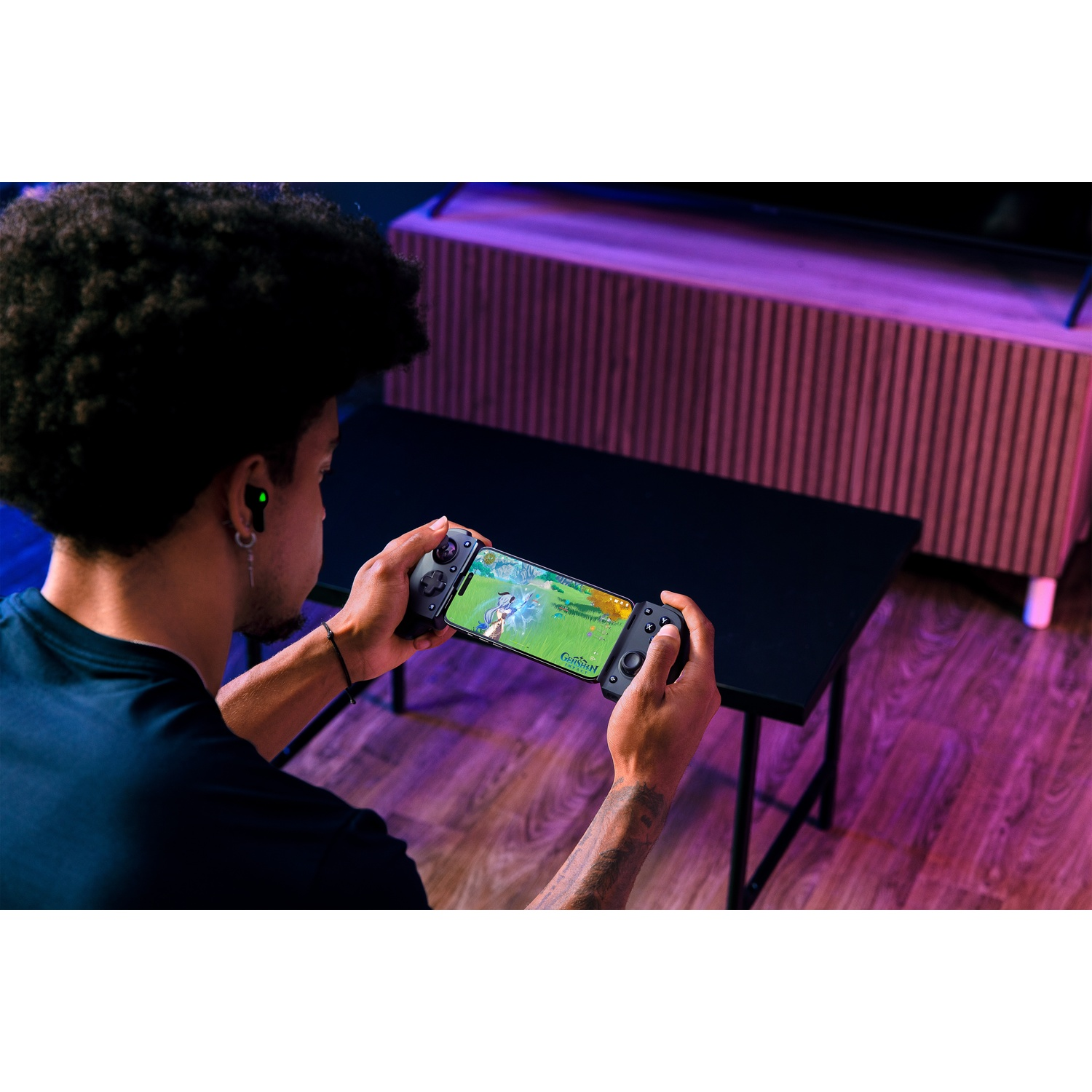 Een persoon speelt een spel op een telefoon die is aangesloten op een controller. De scène is binnen, met een tafel en een patroonmuur.