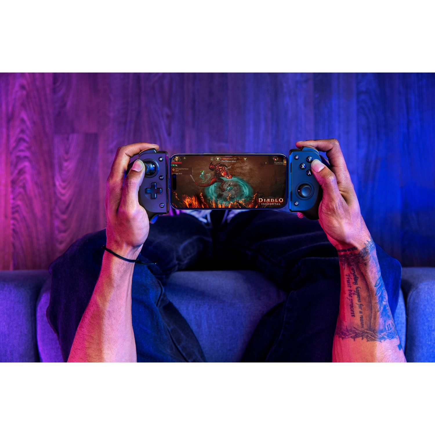 Een persoon speelt Diablo Immortal op een telefoon die is aangesloten op een gamecontroller. De persoon zit op een bank.